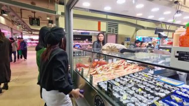 Müşteriler Melbourne balık pazarında taze deniz ürünlerini karıştırıp seçiyorlar. Parlak ışıklandırma, canlı bir atmosferde istiridye ve yengeçleri ön plana çıkarır.