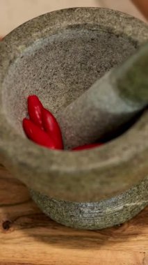 Eller kırmızı biber ve sarımsak ezer taş bir havanda, canlı bir mutfak sahnesi yaratır.