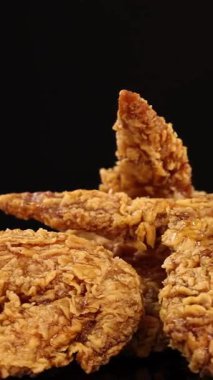 Altın, kızarmış tavuk kanatları stüdyo ışıkları altında yumuşak bir şekilde döner, çıtır çıtır bir dokuyu vurgular ve yavaş kamera hareketleriyle temiz, karanlık bir arkaplan karşısında iştah açıcı detaylar