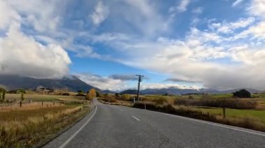 Bir araç sonbahar tarlalarında dolambaçlı kırsal bir yolda dolaşır ve durur, tepeler ve dağlarla çevrilidir dramatik, parçalı bulutlu gökyüzü altında doğal gün ışığı ile.