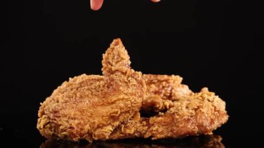 Bir el uzanıyor ve kızarmış tavuk kanadını ağır çekimde ağır çekimde siyah arka planda dramatik bir ışıklandırma ile kaldırıyor.