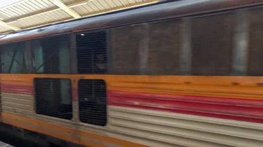 Renkli vagonları olan durgun bir yolcu treni, gün ışığında kapalı bir platformda dış detayları ve pencere görüntülerini pürüzsüz yanal kamera hareketiyle vurguluyor.