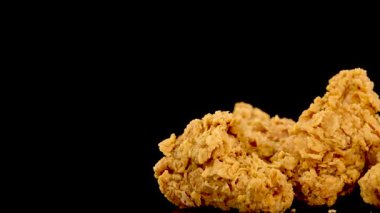 Bir el, parlak siyah bir yüzey üzerindeki bir yığın altın renginde kızarmış tavuk parçası seçer, dramatik stüdyo ışıkları ve yavaş çekim etkisi ile