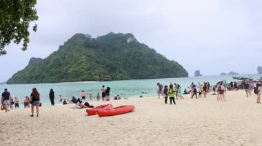 Kalabalık, turne tekneleriyle kumlu sahilde toplanıyor.