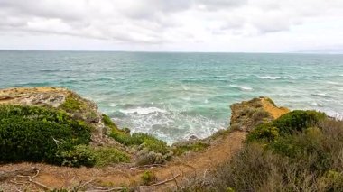 Aireys Körfezi 'ndeki bulutlu gökyüzünün altında kayalıklara çarpan dalgalar sakin bir sahil manzarası yaratıyor.