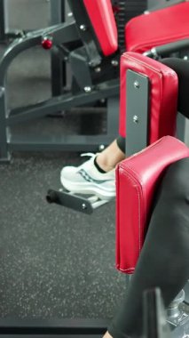 Atletik giyimli bir adam, iyi ışıklandırılmış bir spor merkezinde kalça addüksiyon makinesi kullanıyor. Düzenli kamera çerçeveli, kontrollü bacak hareketlerini gösteriyor.