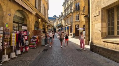 İnsanlar alışveriş yapıyor ve güneşli bir pazarda yürüyor.