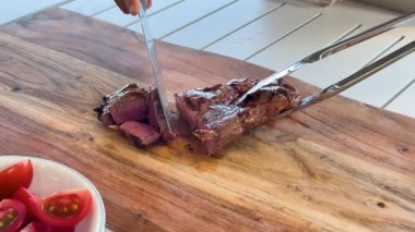 Tahtada pişmiş biftek dilimliyorum.