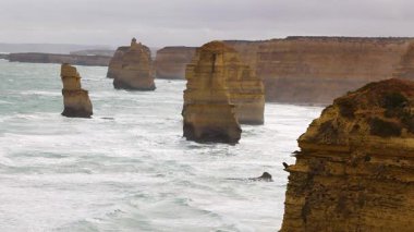 12 Havari kaya oluşumları, Avustralya 'nın Port Campbell şehrinde bulutlu gökyüzü altında çalkantılı okyanus dalgalarına karşı duruyor.