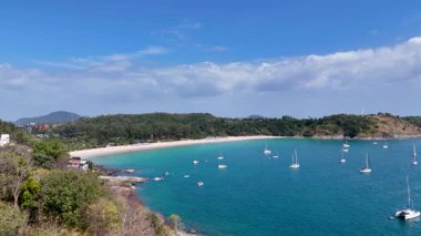 İnsansız hava aracı görüntüleri Phuket, Tayland 'da güneşli gökyüzünün altında demirli tekneler, yemyeşil yemyeşil ve berrak mavi suları gösteren sakin bir koy yakalıyor.