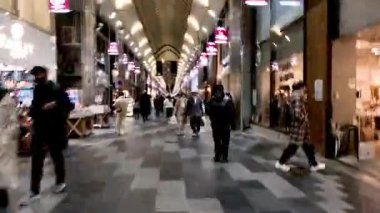 İnsanlar hareketli bir alışveriş salonunda yürüyor.