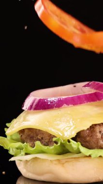 Susamlı bir çörek, salatalı, domatesli, soğanlı ve peynirli sığır etli bir çizburgerin üzerine düşer.