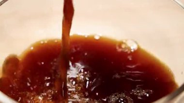 Bir bardağa doldurulan kahvenin yakın plan çekimleri, siyah arka planda zengin köpükler ve kabarcıklar yaratıyor.