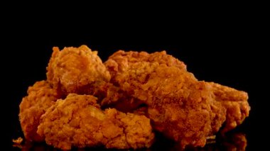 Altın kızartılmış tavuk parçaları ağır çekimde ağır çekimde siyah arka plana karşı baharatlarla serpiştiriliyor. Dokular, baharatlar ve dramatik stüdyo ışıkları vurgulanıyor.