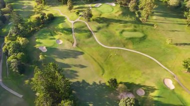 İnsansız hava aracı görüntüleri, güneş ışığı altındaki çimenli, sığınaklı ve ağaçlı yemyeşil bir golf sahası yakalıyor.