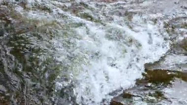 Dinamik bir akıntı yosunlu kayaların üzerinden akar, kabarcıklar yaratır ve doğal ışıkta su sıçratır.