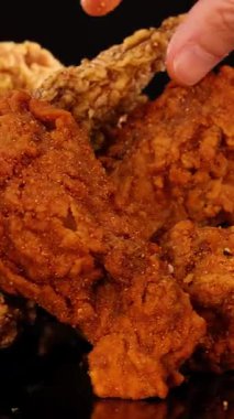 Bir el uzanıp çeşitli kızarmış tavuk kanatları, but ve nuggetları alır. Sıcak stüdyo ışıkları altında, karanlık, minimal arka planda.