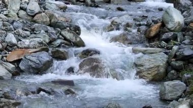 Açık dağ akıntısı, açık havada geniş kaya ve kayaların üzerinden hızla akar. Statik kamera, doğal gün ışığı, net ayrıntı.