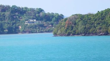 Yatlar, bereketli Phuket tepelerinin yakınındaki turkuaz sularda süzülüyor. Parlak gün ışığı huzurlu, resimli sahil manzarasını güçlendirir.