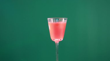 Yeşil arka planda dekoratif garnitürlü pembe bir kokteyl. Parlak ışıklandırma canlı renkleri güçlendirir