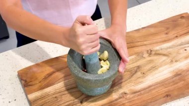 Eller sarımsak ve kırmızı biberi harç ve ahşap bir kesme tahtasının üzerinde, parlak bir şekilde öğütür. Mutfak ışıkları bile sabit bir kamera açısıyla açılıdır.