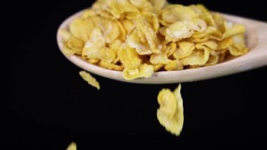 Mısır gevreği yavaş çekimde bir kaşıktan siyah bir arka plana doğru düşer, dokuyu ve hareketi vurgular.