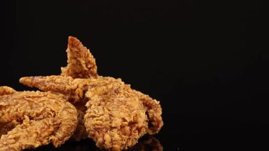 Kızarmış tavuk kanatları yumuşak stüdyo ışıkları, çıtır çıtır dokular ve iştah açıcı detaylarla aydınlatılmış parlak siyah bir yüzey üzerinde pürüzsüz bir şekilde döner.