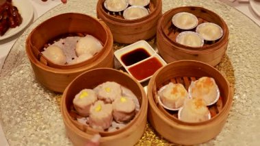 Eller, sıcak aydınlatma altında soslu bir masada bambu buharlı tencerelerden loş suşi seçiyor.