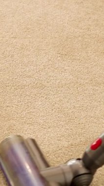 Elektrikli süpürge parlak bir odada bej bir halıda hareket eder. Etkili temizlik hareketleri sergiler.