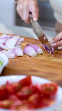 Ahşap bir tahtanın üzerinde arpacık soğanları dilimleyen eller ve yanında taze sebzeler.