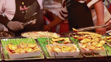 Tedarikçiler, hareketli ışıklandırmalı ve hareketli bir pazarda yemek hazırlamak ve servis etmek için maşa ve çubuk kullanırlar.