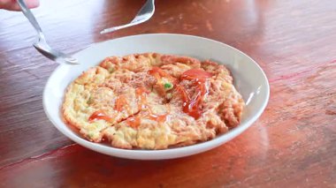 Bir insan kırmızı biber soslu Tayland usulü omlet seviyor, çatal ve kaşıkla parlak bir ayar kullanıyor.