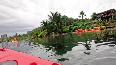 Kayakçılar yemyeşil, manzaralı bir su geçidinde yol alırlar.