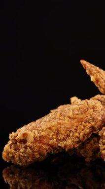 Kızarmış tavuk kanatları stüdyo ışıkları altında pürüzsüz bir şekilde döner, çıtır çıtır dokuları ve sulu detayları ince yansımaları olan temiz, siyah bir zemin üzerinde vurgular.