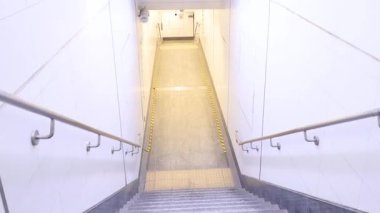 Temiz, beyaz duvarları ve metal parmaklıkları olan iyi ışıklandırılmış, boş metro merdivenlerini gösteren bir çerçeve dizisi.