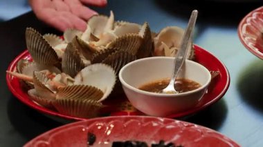 Kırmızı tabakta deniz tarağı ve acı sos bulunan canlı bir deniz ürünleri tabağı, canlı bir yemek ortamında yakalandı.