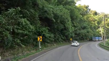 Ağaçlarla çevrili dolambaçlı bir yolda araçlar geziniyor.