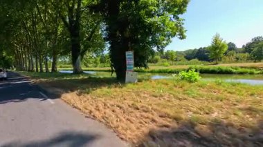 Sakin bir kanalın yanında ağaçlarla kaplı bir yol.