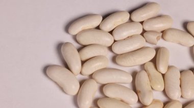 Beyaz fasulye çekirdekleri bir tabağa yerleştirilmiş, makro detaylarda, tutarlı ışıklandırma ve en az kamera hareketiyle yakalanmış.