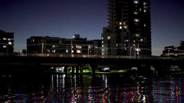 Aydınlatılmış binaları ve su üzerindeki yansımaları olan şehir manzarası