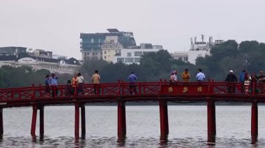 İnsanlar suyun üzerinde kırmızı bir köprüde yürüyor.