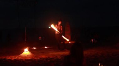 A performer twirls fire on a sandy beach in Phuket, Thailand, creating a mesmerizing display against the night sky