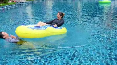 İki kişi Yengeç havuzunda güneşli bir günün tadını çıkarırken, biri şişme bir halkada yüzerken diğeri yakınlarda yüzüyor.