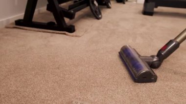 Elektrikli süpürge halı kaplı bir spor salonunda hareket eder. İyi ışıklandırılmış bir ortamda temizlik ve verimliliği ön plana çıkarır.