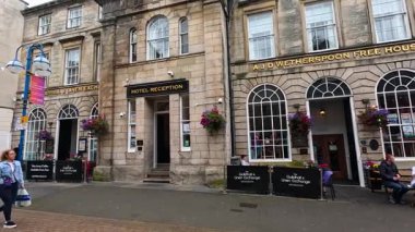 İnsanlar dükkanların ve otelin önünden geçiyor.