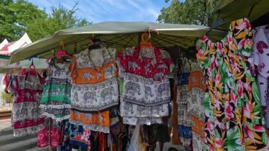 Canlı fil temalı giysiler Kanchanaburi, Tayland 'da bir pazar çadırının altında asılı. Gün ışığı, düz kamera hareketiyle yakalanan desenli gömlek ve elbiseleri aydınlatır.