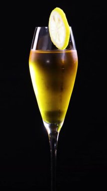 Limonla süslenmiş bir kokteyl, parlak rengini ve zarif sunumunu vurgulayarak, koyu bir zemin üzerinde sorunsuzca döner.