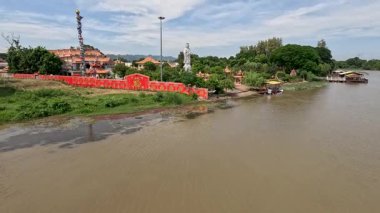 Drone kamerası Kwai Nehri 'nin yukarısında canlı bir nehir kenarı tapınağı, kırmızı duvarlar, yemyeşil yemyeşil ve Kanchanaburi, Tayland' da dramatik bir gökyüzü gösteriyor.