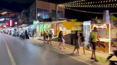 Tuk-tuk yolculuğu Phuket, Tayland 'daki hareketli gece hayatı ve renkli sokak manzaralarını canlı dükkanlar ve canlı ışıklandırmalarla yakalıyor.