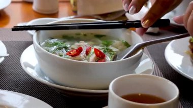 Yemek çubuğu ve kaşıkla erişte çorbası içen biri.